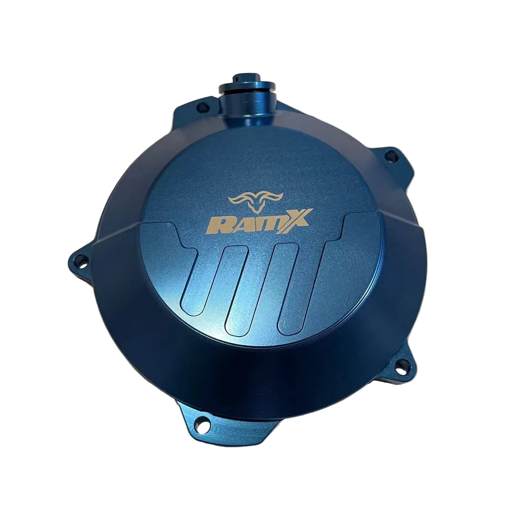 A blue anodized metal motorcycle engine cover with a gold RAMX logo, photographed from a top-down angle on a beige background.